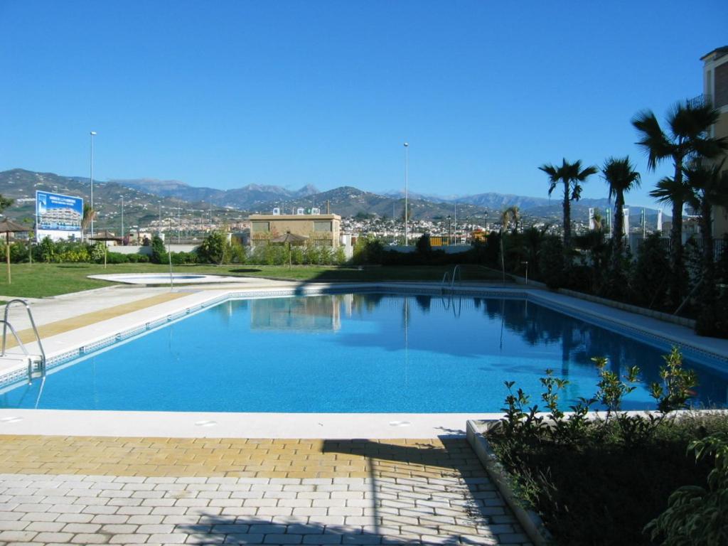 a large blue swimming pool with a city in the background at TERRASOL AZUCARERA ATICO LUJO in Torre del Mar