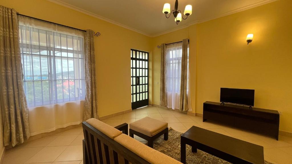 a living room with a couch and a tv and windows at OLMOTI SUITES in Arusha