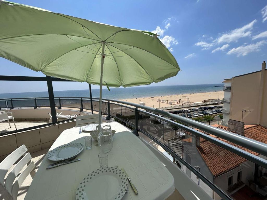 une table avec un parasol vert sur un balcon avec une plage dans l'établissement Appartement 2 pièces avec balcon, vue mer latérale - FR-1-224C-301, à Saint-Jean-de-Monts