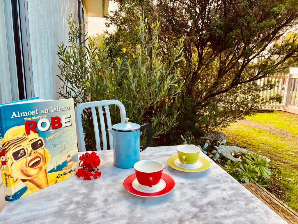 a table with two cups of coffee and a book at No 34 Where Nature Meets the Ocean Pet Friendly in Robe