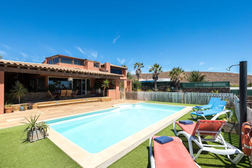 a swimming pool in a yard with chairs and a house at Home2Book Ocean Surf House Fuerteventura in La Oliva