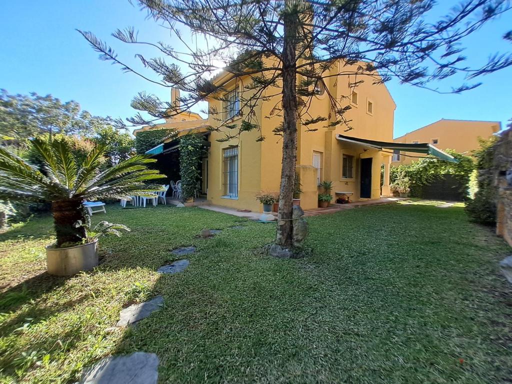 Una casa con un patio de césped con árboles en el frente. en Casa playa El Ancla Puerto Santa María, en El Puerto de Santa María