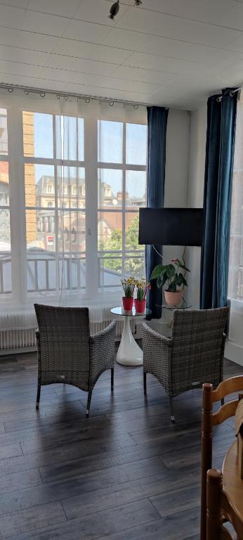een woonkamer met 2 stoelen, een tafel en ramen bij appartement du caractère in Elbeuf