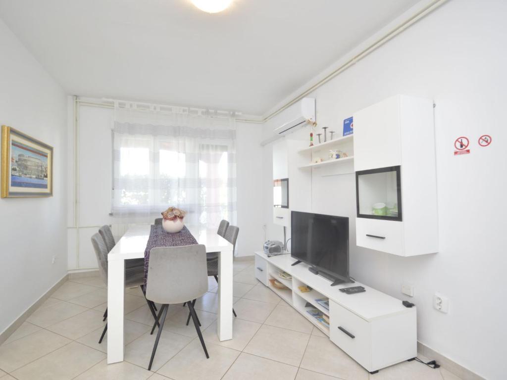 a white dining room with a table and a tv at Apartment Bozac - PUL480 by Interhome in Šikići