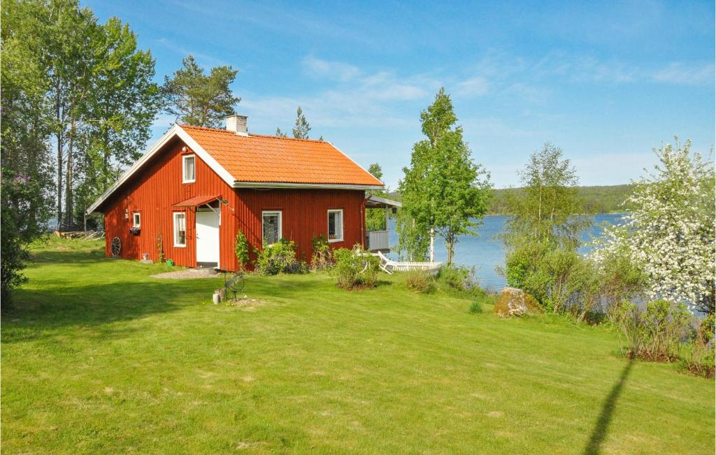 a red house on a lawn next to a lake at Cozy Home In motfors With Lake View in Åmotsfors