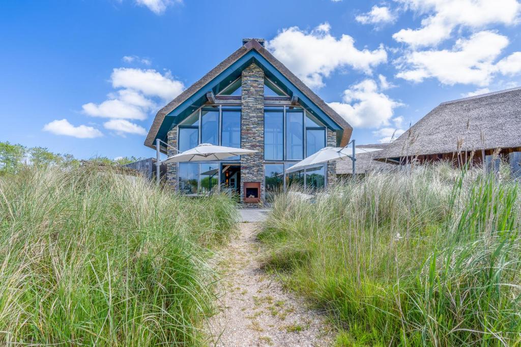 a house with glass windows and a pathway through tall grass at Buytenplaats Villa 193 in De Koog