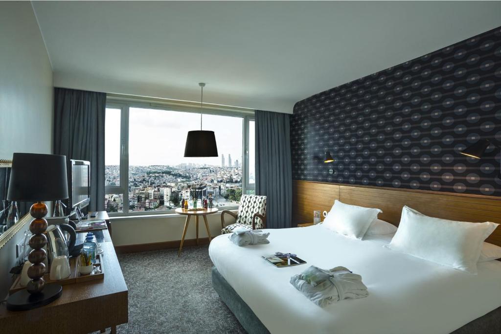 イスタンブールにあるザ マルマラ ペラのベッドと大きな窓が備わるホテルルームです。