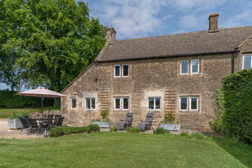 a large brick house with chairs and an umbrella at Bill's Cottage in Northleach