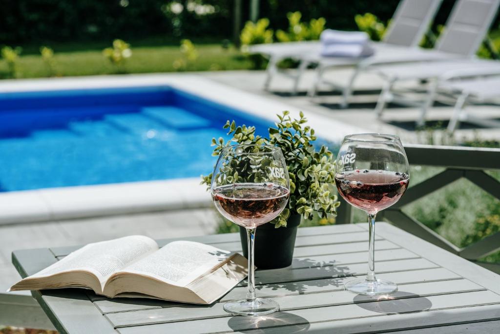 two glasses of wine and a book on a table by a pool at Old Town Zagreb Airport in Velika Gorica