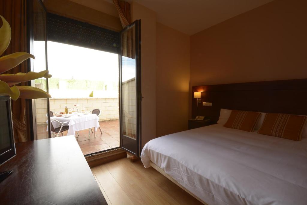 a bedroom with a bed and a balcony with a table at Hotel Campos de Castilla in Soria