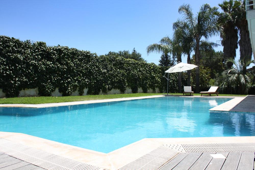 a large swimming pool with an umbrella and a chair at Ara Town House in San Giovanni la Punta