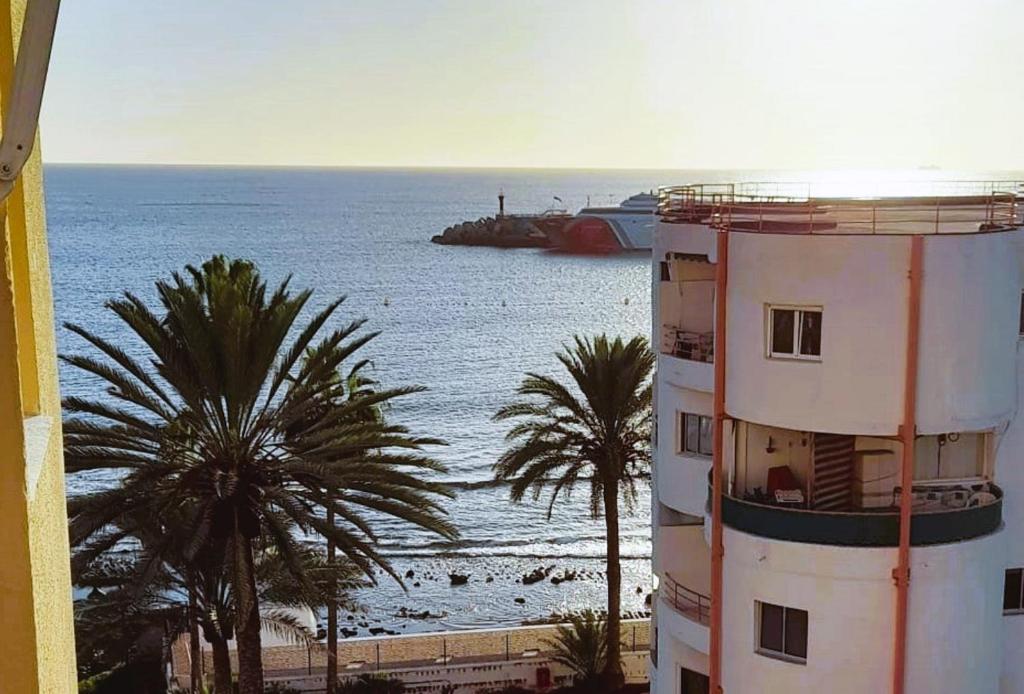 a building with palm trees next to a body of water at DREAMY SUNSET, SeaFront, Direct Access To The Promenade,Wifi,Free Parking in Los Cristianos