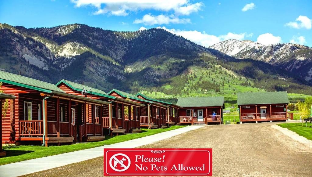 a row of wooden buildings with mountains in the background at Wolf Den Log Cabin Motel and RV Park in Thayne