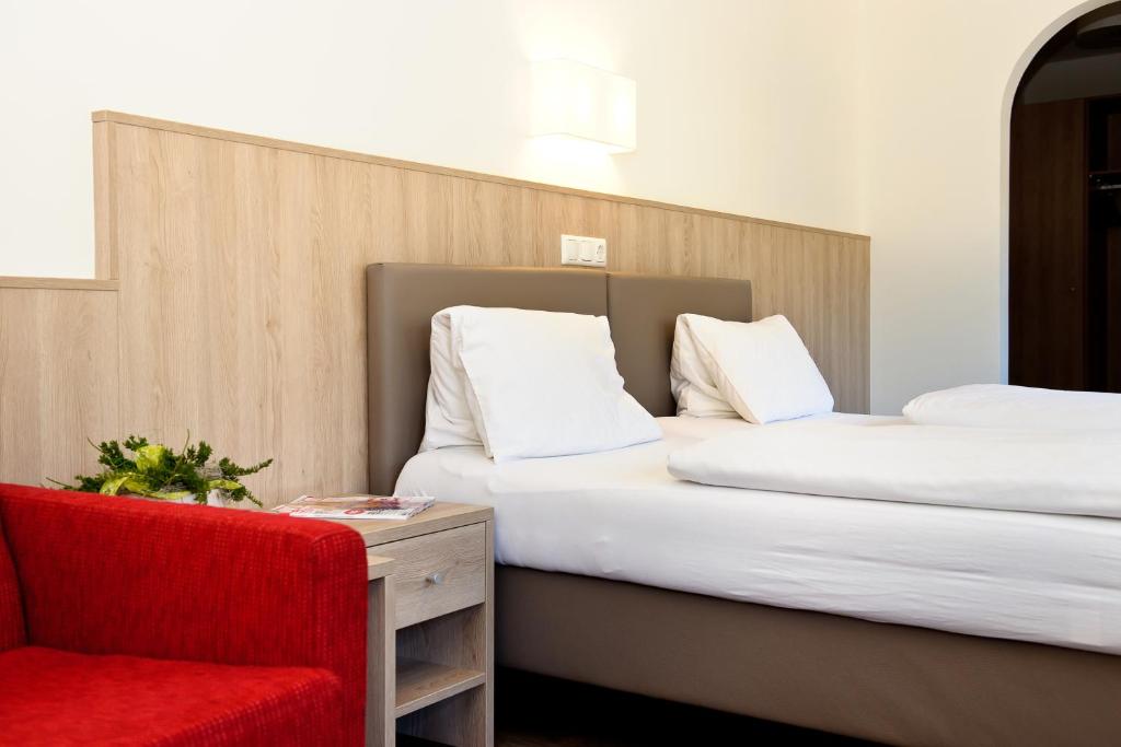 two beds in a hotel room with a red chair at Gasthaus Bacher in Sankt Johann im Pongau