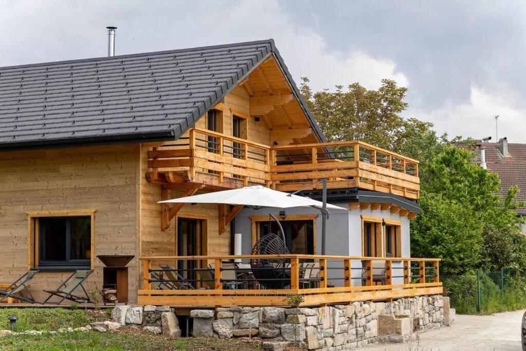 a wooden house with a deck and an umbrella at Chalet au coeur du Jura à 5min de la plage de Clairvaux 