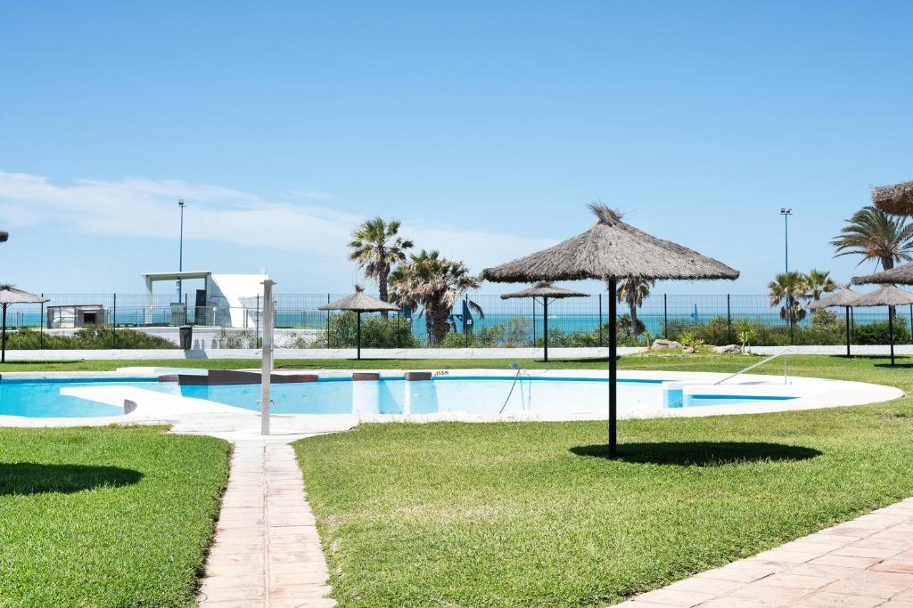 a swimming pool with an umbrella and the ocean at Barrosa Primera línea de playa in Chiclana de la Frontera