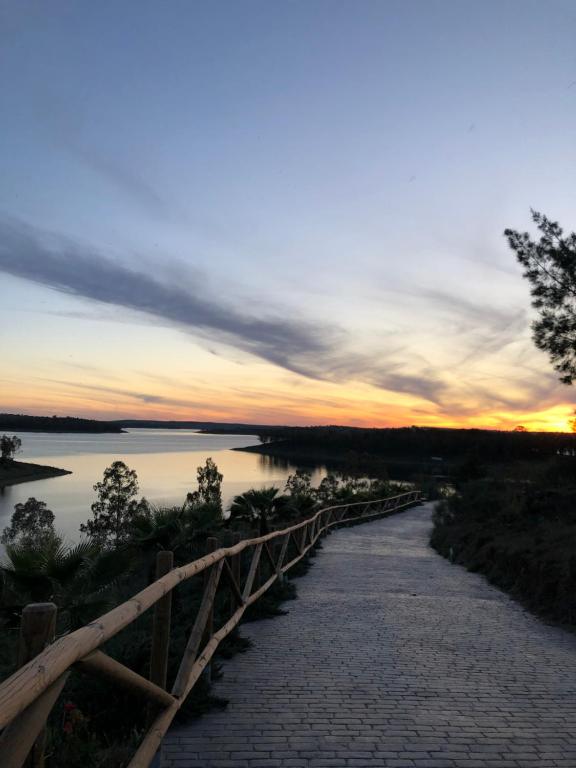 un pont sur une rivière avec un coucher de soleil en arrière-plan dans l'établissement Casa Rural encantos de Orellana, à Navalvillar de Pela