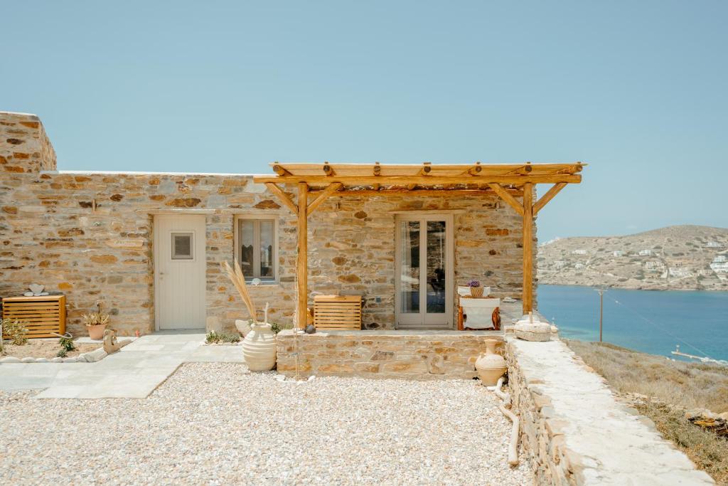 una casa de piedra con una pérgola de madera junto al agua en Heliopetra Punta, en Ios Chora