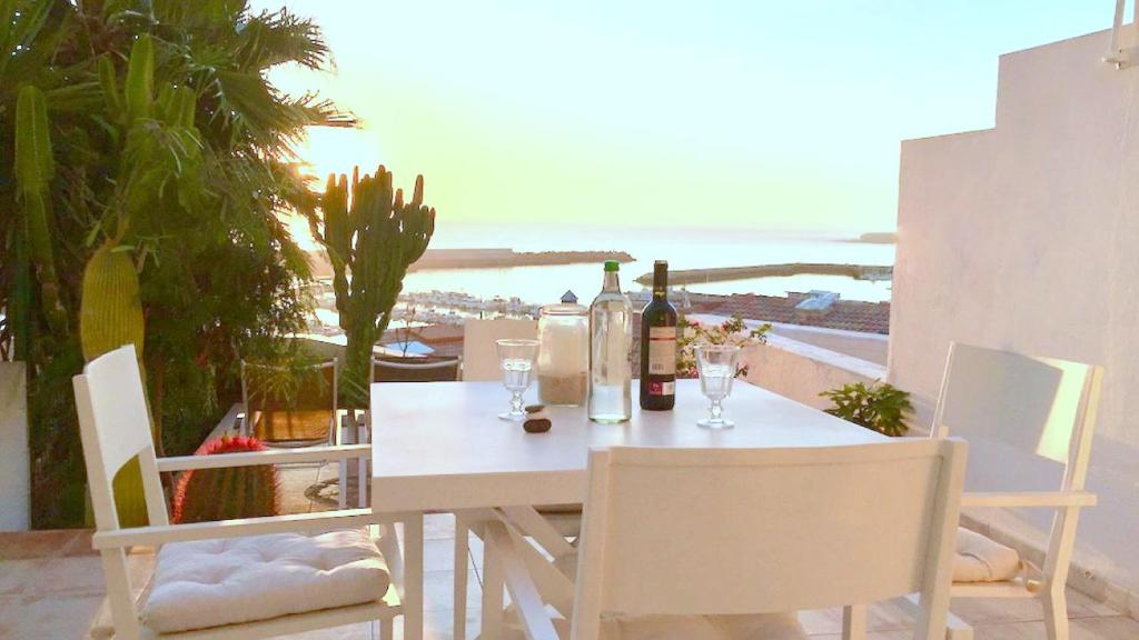 una mesa y sillas blancas con botellas de vino y copas en Salinas, en Morro del Jable