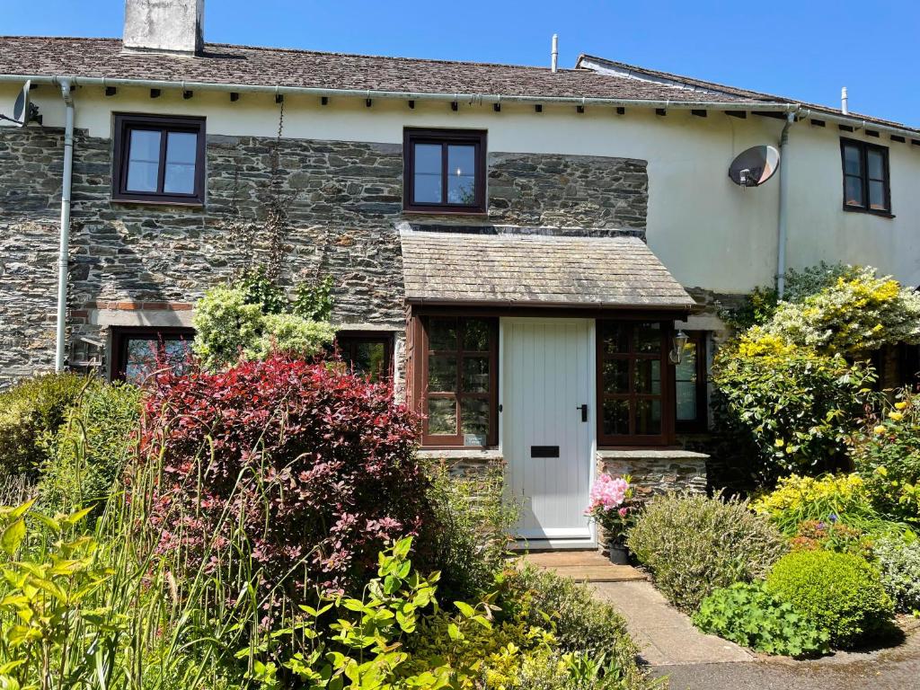 a stone house with a white door and some bushes at Sandpiper Cottage in Salcombe