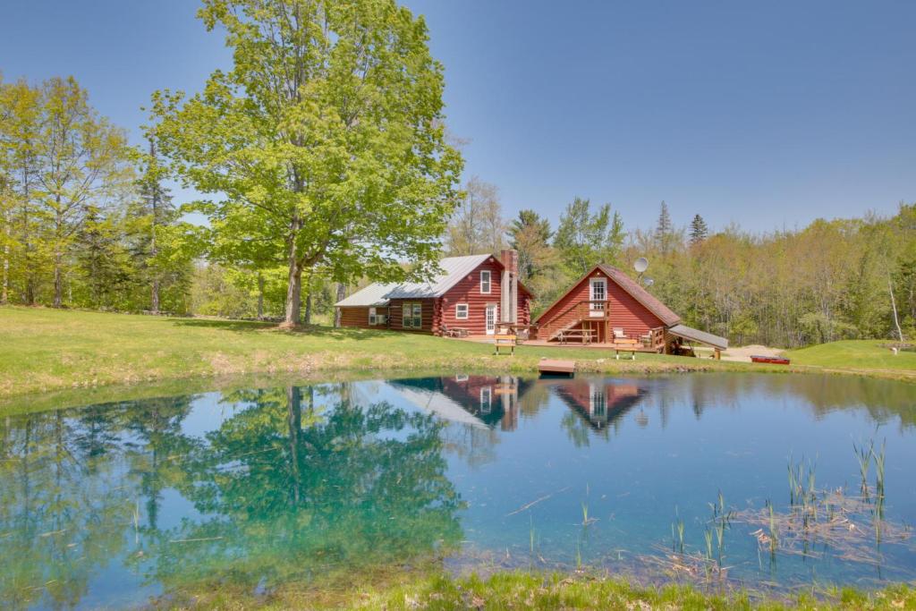 una cabaña roja con un lago frente a ella en Unique Maine Log Cabin with Trout Ponds and Sauna! 