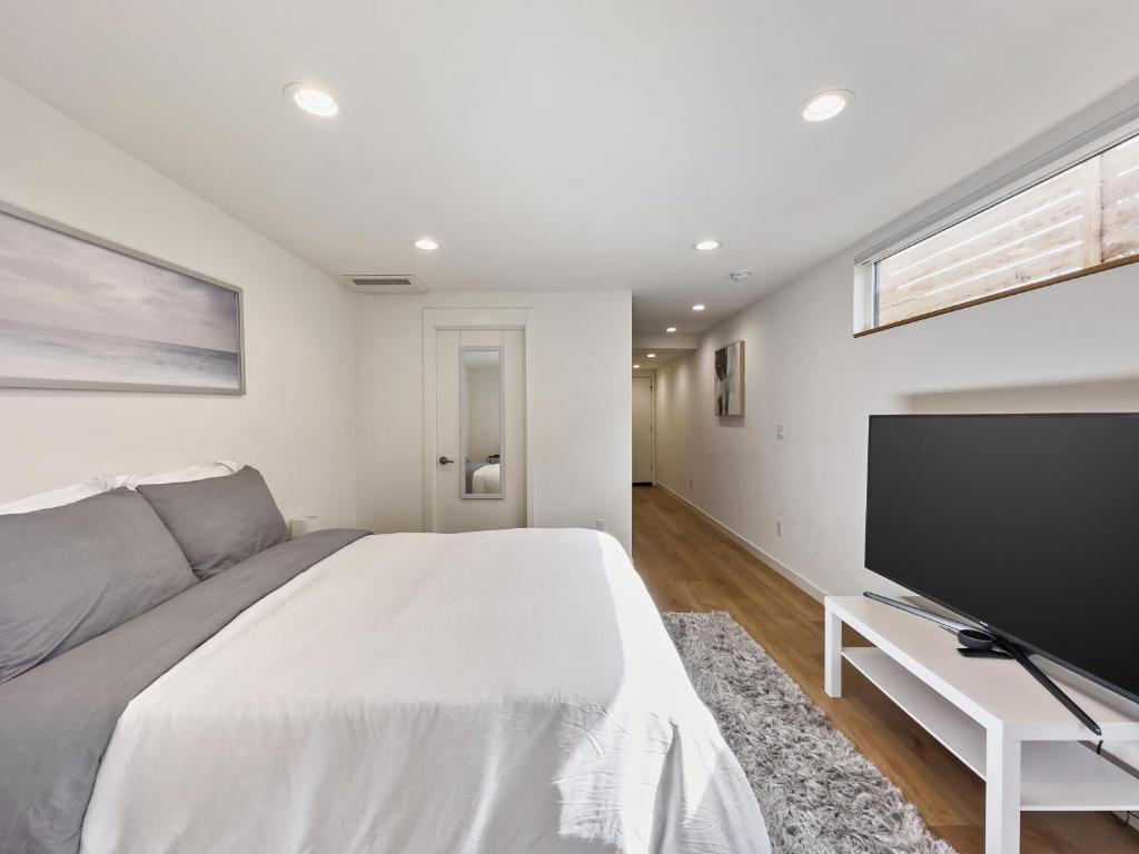 a white bedroom with a large bed and a flat screen tv at Modern apartment near light rail in Seattle