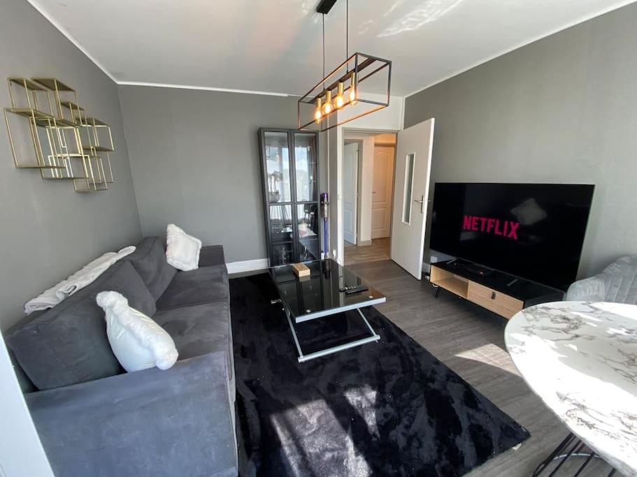 a living room with a gray couch and a television at Appartement familial Wifi Netflix Amazon Prime in Saint-Cyr-lʼÉcole