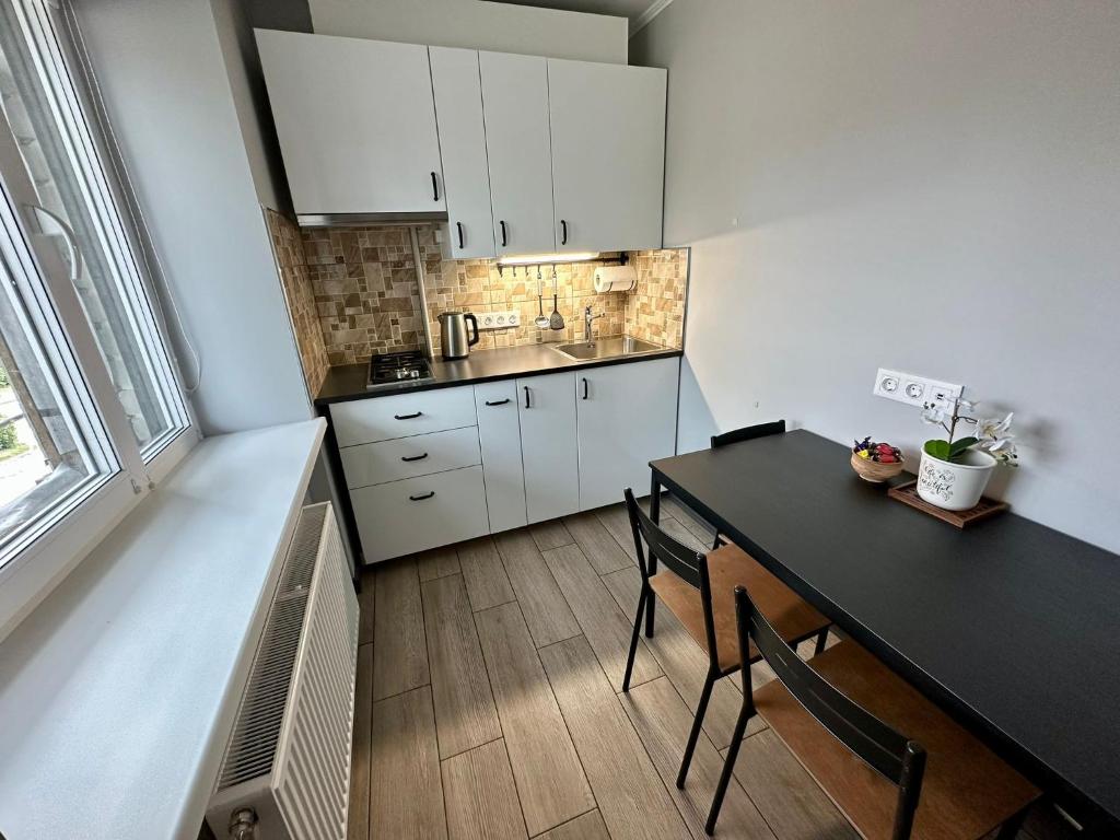 una cocina con armarios blancos, mesa negra y sillas en Swan City Family Apartment en Gulbene