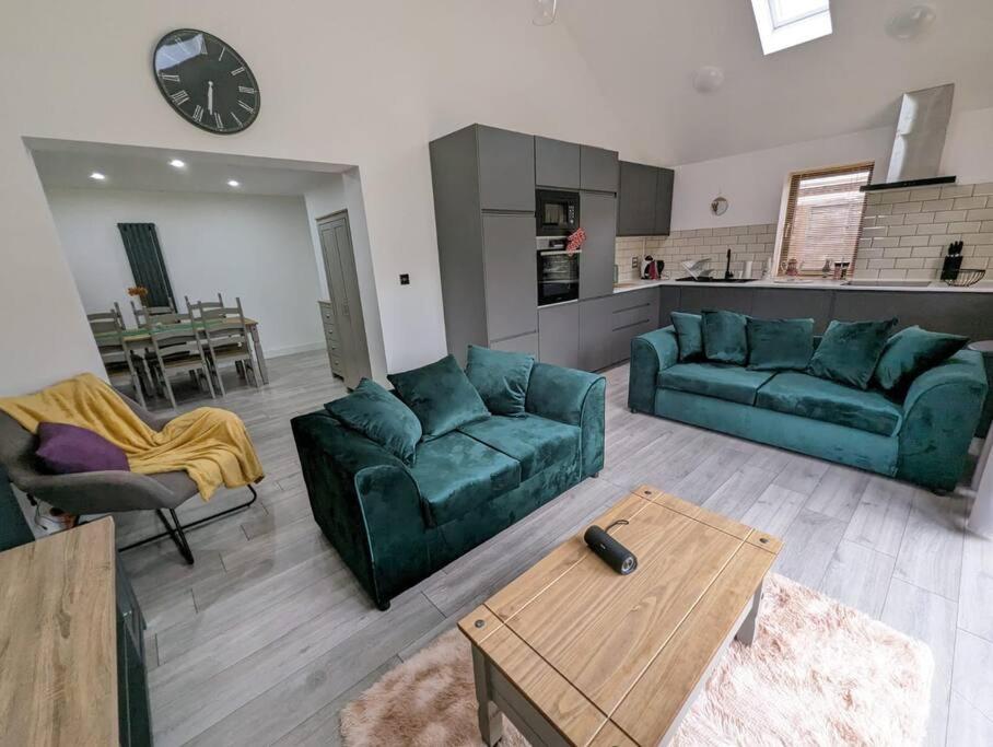 a living room with two green couches and a kitchen at 7 Guests - 4 Bedroom - Free Wi-Fi - Kettering in Kettering