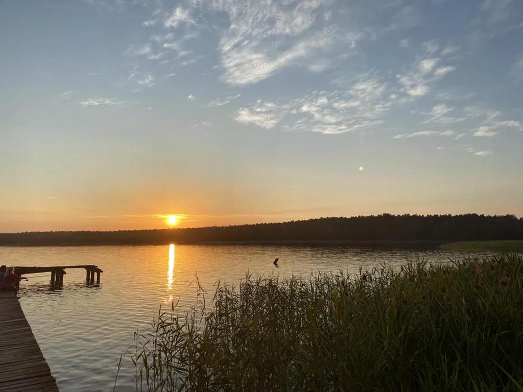 un coucher de soleil sur un lac avec un quai en bois dans l'établissement Domek Letniskowy nad Jeziorem, Las, Mazury, à Wiartel Mały