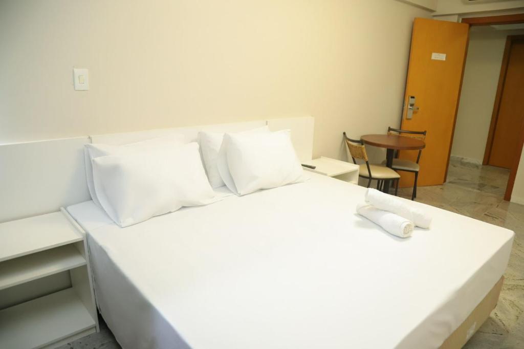 a white bed with white pillows and a table at Rede Andrade Pampulha in Belo Horizonte