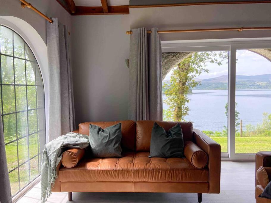 a brown couch in a living room with a large window at Sunset Cottage in Kenmare