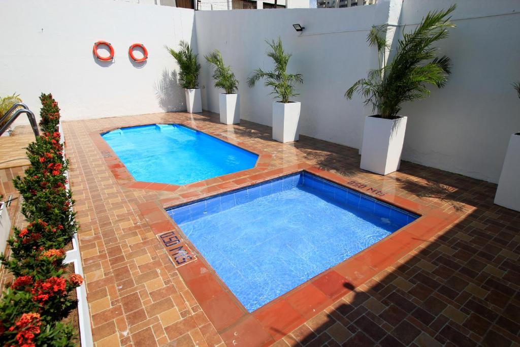 a large swimming pool in a courtyard with potted plants at Hotel Rodadero Inn By GEH Suites in Santa Marta