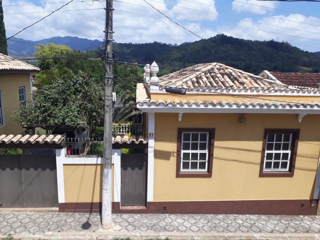 una casa amarilla con una valla y montañas al fondo en Mini Casarão en São Bento do Sapucaí