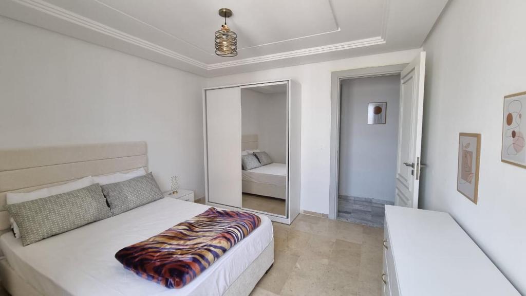 a white bedroom with a large bed and a mirror at Le 6éme in Sousse