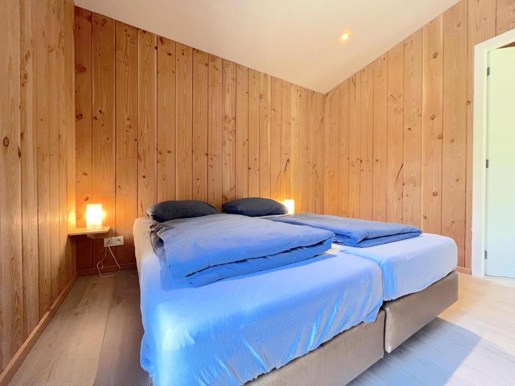 a bedroom with wooden walls and two beds with blue pillows at De Goolder in Bocholt