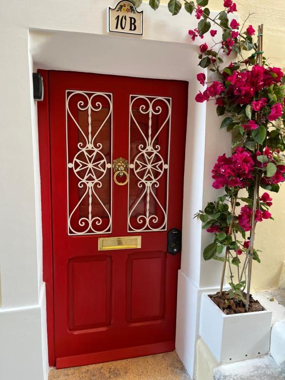 une porte rouge dans un mur blanc avec des fleurs roses dans l'établissement San Biagio Steps, à La Valette