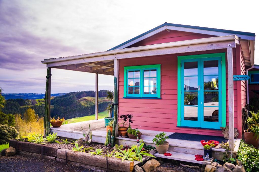 ein kleines rosafarbenes Haus mit blauen Fenstern und Pflanzen in der Unterkunft Fridas Accommodation in Raglan