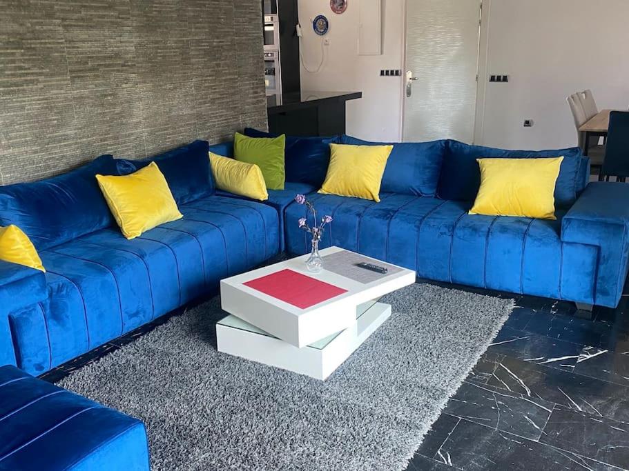 - un canapé bleu avec des oreillers jaunes dans le salon dans l'établissement Superbe appartement meublé à louer avec piscine, à Harhoura