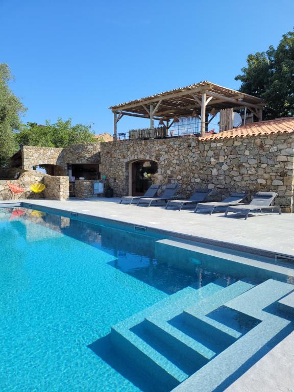 a swimming pool with chairs and a stone building at La Bergerie in LʼÎle-Rousse