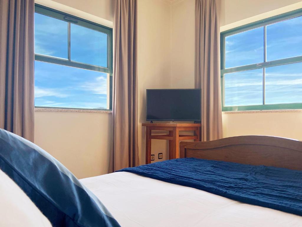 um quarto com uma cama e uma televisão e duas janelas em Vinhais Hotel em Vinhais
