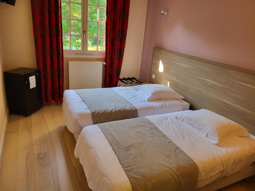 a bedroom with two beds and a window with red curtains at Hôtel La Flambée in Bergerac