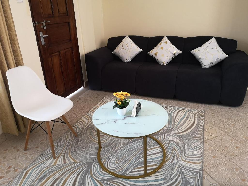 Diani Ocean View Apartment في أوكوندا: غرفة معيشة مع أريكة سوداء وطاولة وكرسي أبيض