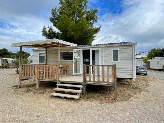 une petite maison avec une véranda et un parasol dans l'établissement Mobil-home 6 personnes - Camping La Falaise 4* / Piscine / Club enfants / SPA / Restaurant / Animations, à Narbonne