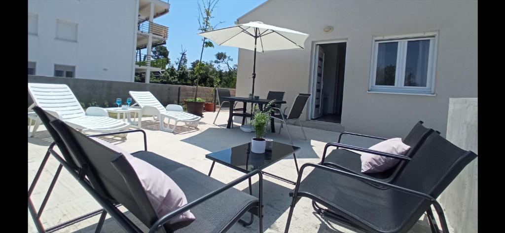 eine Terrasse mit Stühlen, einem Tisch und einem Sonnenschirm in der Unterkunft Apartman Punta Radman in Petrcane