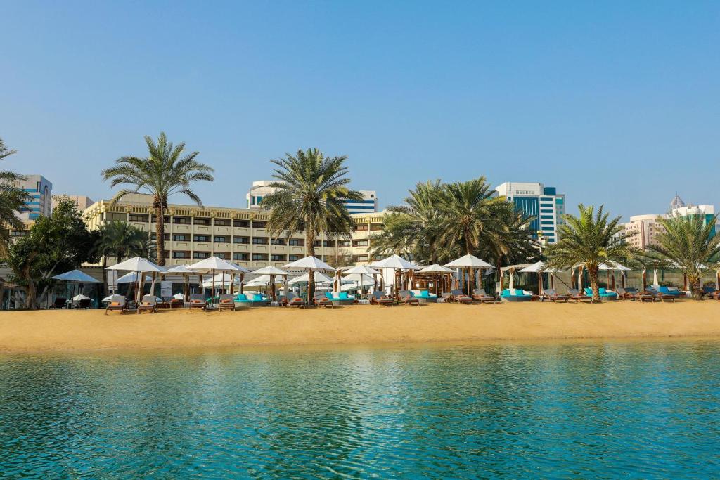 a beach with umbrellas and palm trees and a hotel at Le Meridien Abu Dhabi in Abu Dhabi