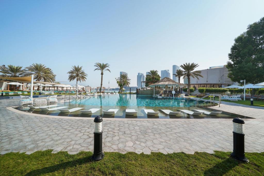 a large swimming pool with lounge chairs and palm trees at Le Meridien Abu Dhabi in Abu Dhabi