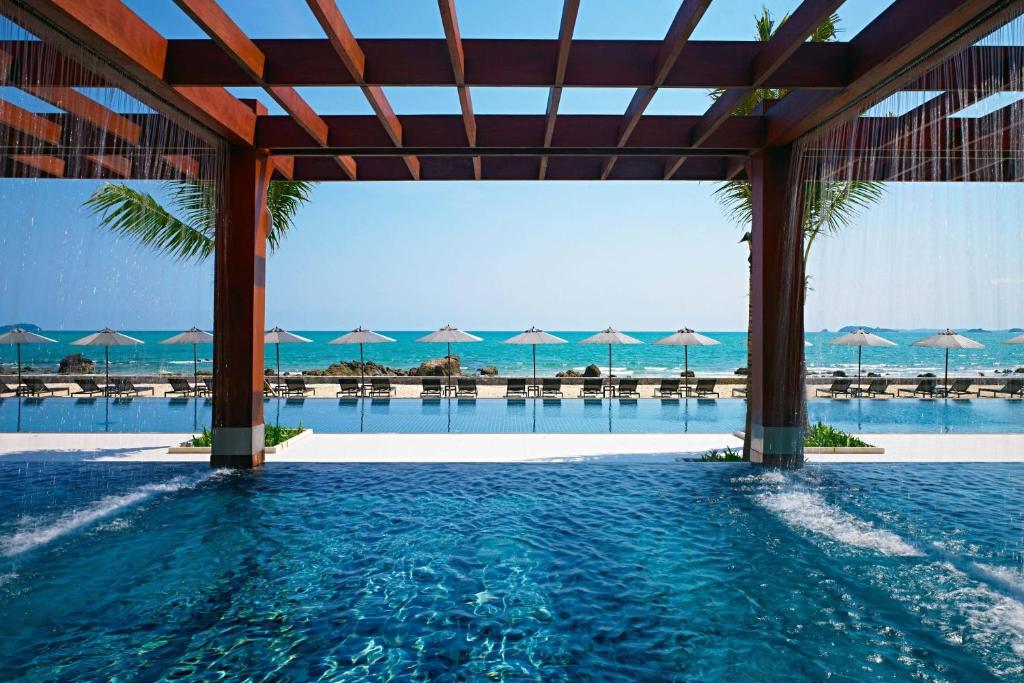 a pool with umbrellas and the ocean in the background at Rayong Marriott Resort & Spa in Klaeng