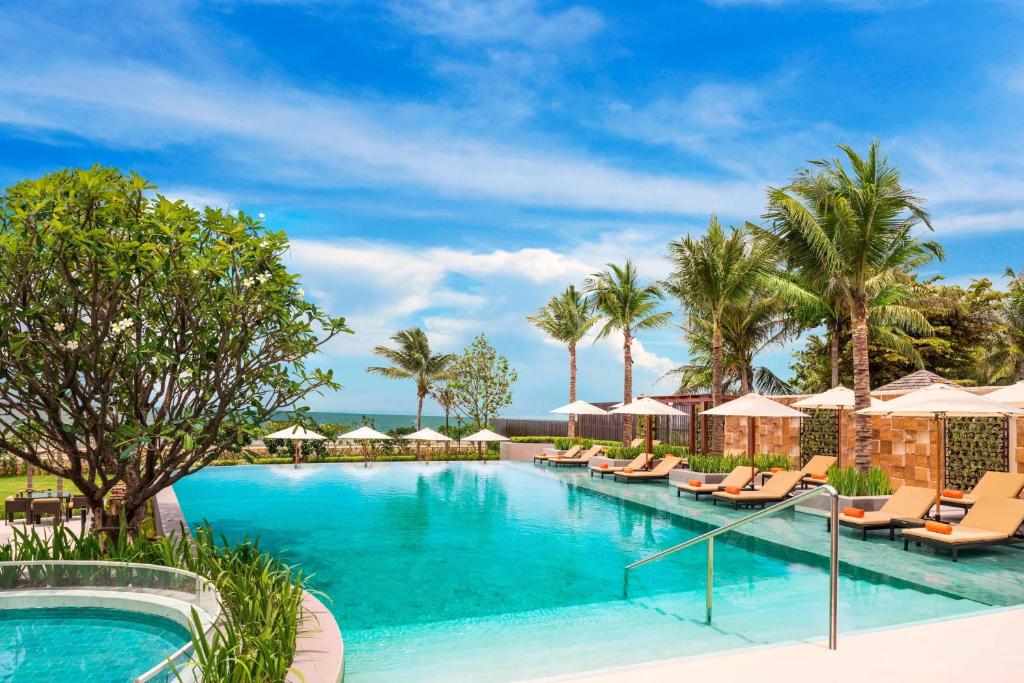 - une piscine avec des chaises et des parasols dans un complexe dans l'établissement Sheraton Hua Hin Pranburi Villas, à Pran Buri