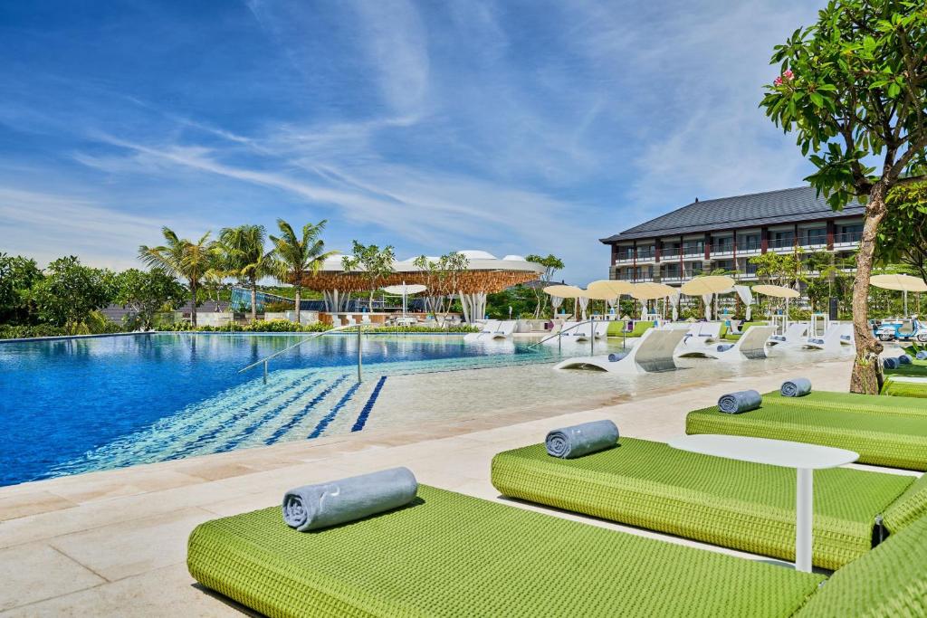 une piscine dans un complexe avec des chaises vertes et un bâtiment dans l'établissement Renaissance Bali Nusa Dua Resort, à Nusa Dua